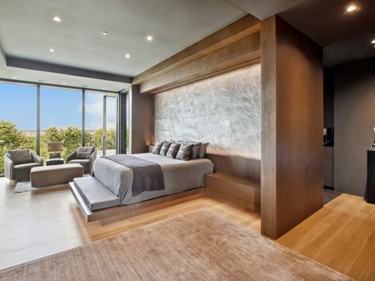 A bright bedroom with a low bed, large windows and a standing lamp